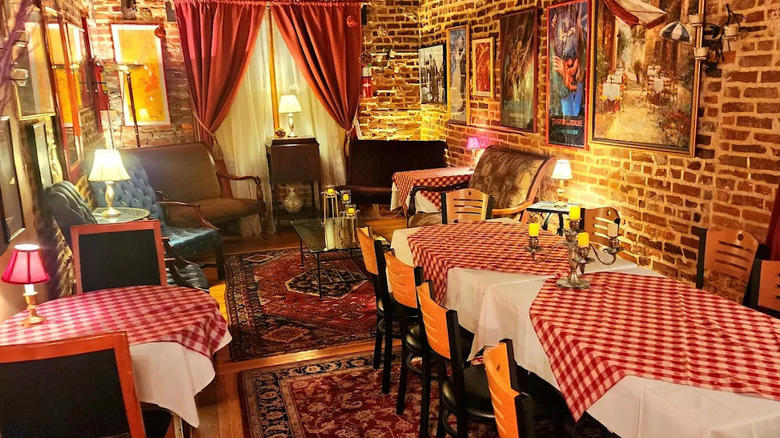 Interior view of Victor Cafe, Philadelphia, of a room with exposed brick walls, artwork, Persian-style rugs, and tables covered with red checked tablecloths with dim lighting