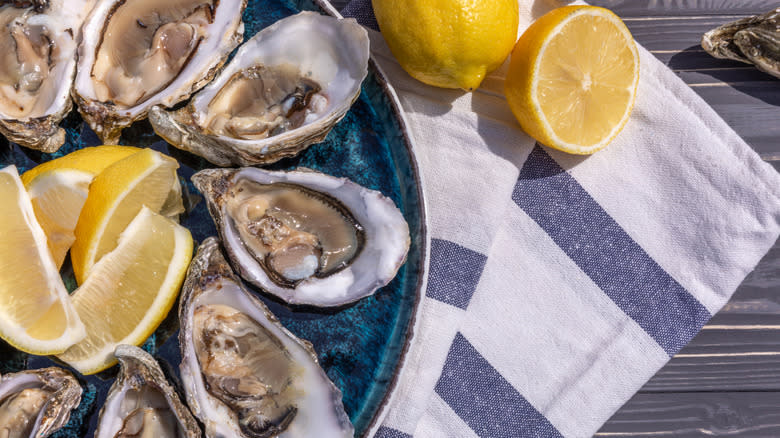 Raw oysters with lemons in sunshine on table with striped cloth.