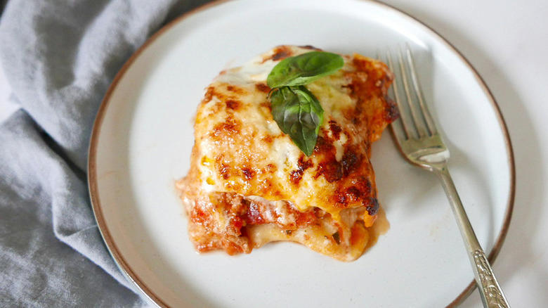 Portion of lasagna on plate, topped with basil leaves
