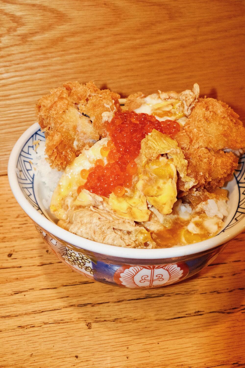 Ikura-topped pork cutlet bowl with egg and rice on a wood counter