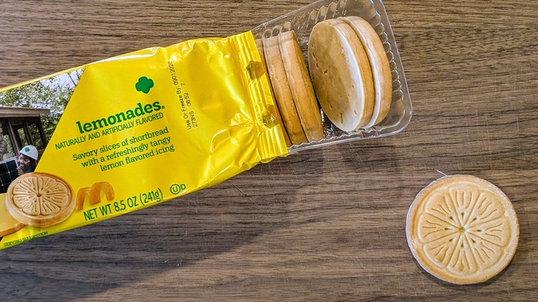An open package of Lemonades next to one cookie outside of the package on a wood board