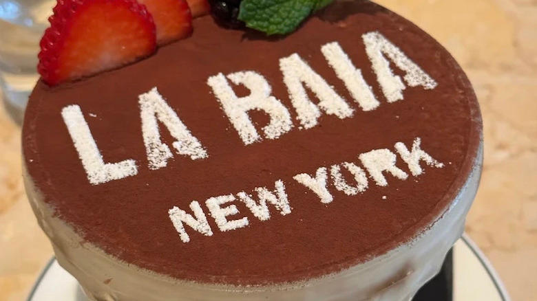 Close up of Tiramisu dessert in a glass dish at Osteria La Baia with "La Baia New York" written on cocoa powder and strawberries visible at the top