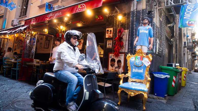 Man drives a Vespa by a pizzeria in Naples, Italy
