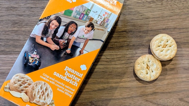 A box of Peanut Butter Sandwich cookies next to two cookies on a wood board
