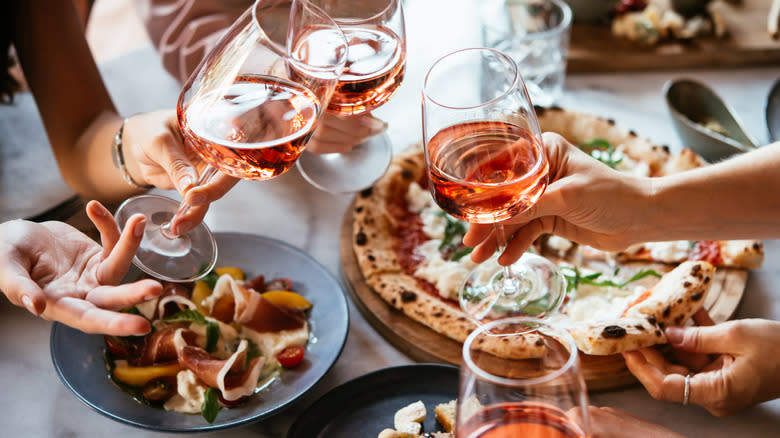four women holding wine glasses with rosé over a table filled with Italian food, like pizza and prosciutto