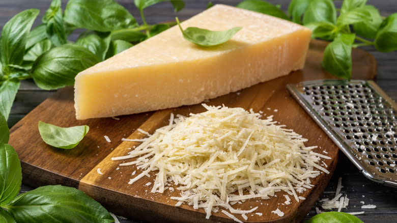 A block of grated parmesan on a wooden board with fresh basil leaves