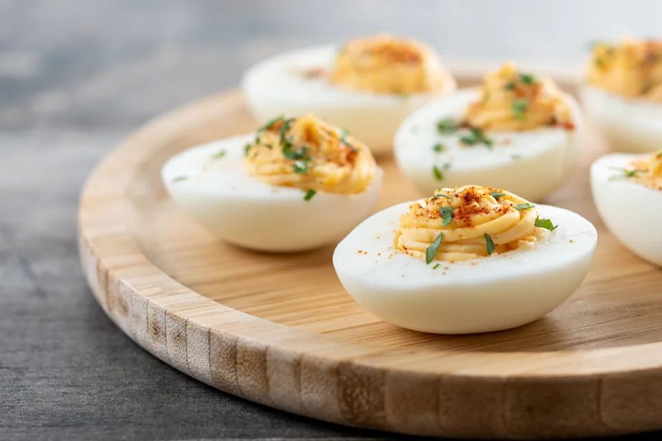 Homemade hard Boiled Deviled Eggs garnished with herbs on wooden table.