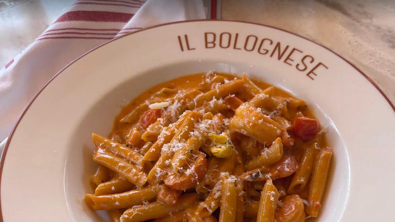 Close-up view of pasta in spicy vodka sauce on marble table in white dish with "Il Bolognese" in red, white and red striped napkin to the left