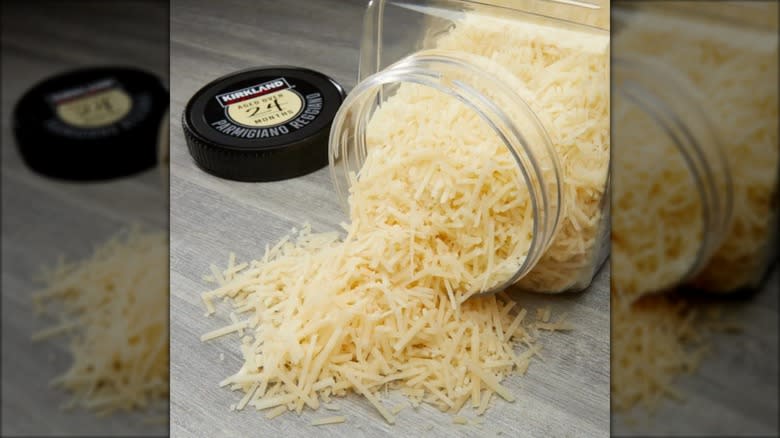 A tub of Kirkland Signature Parmigiano Reggiano shredded cheese, with some cheese piled onto a wooden surface