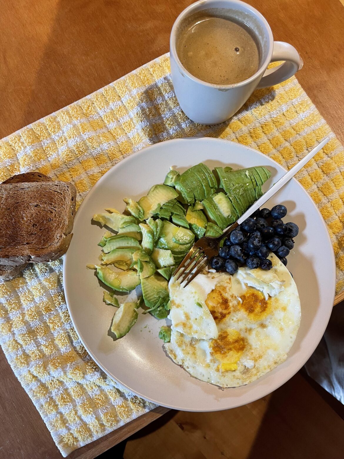Coffee with almond milk, avocado, egg, whole wheat bread toast and blueberries.