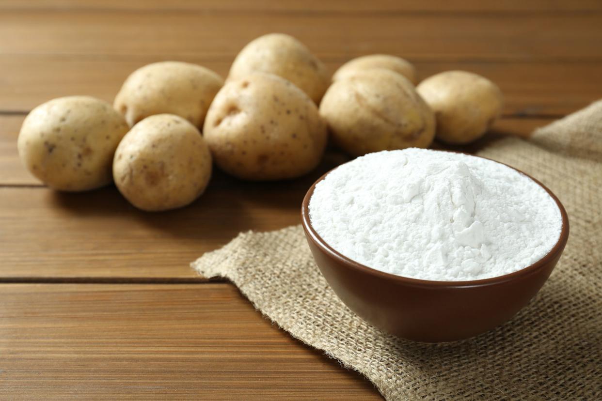 Bowl with starch and fresh potatoes on wooden table, space for text