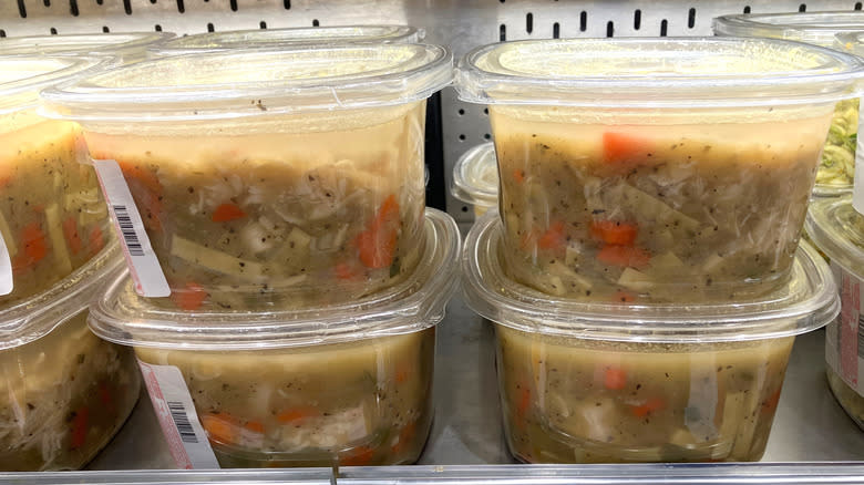 Large chunks of chicken, noodles, and vegetables are visible through clear plastic tubs of Kirkland Signature Rotisserie Chicken Noodle soup on a refrigerated shelf