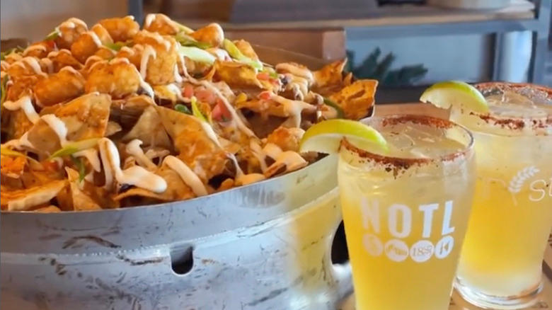 bucket of nachos with sides of sour cream, salsa, extra cheese with two drinks