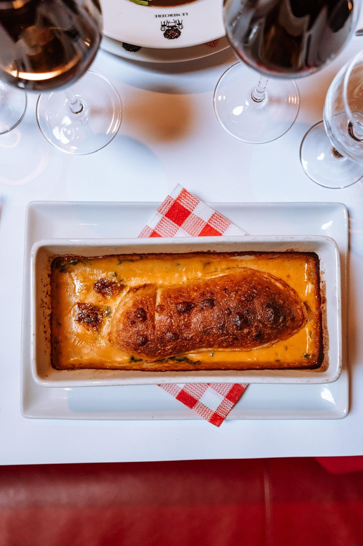 A close-up of a baked, rectangular pie on a table with white linen and red wine glasses.