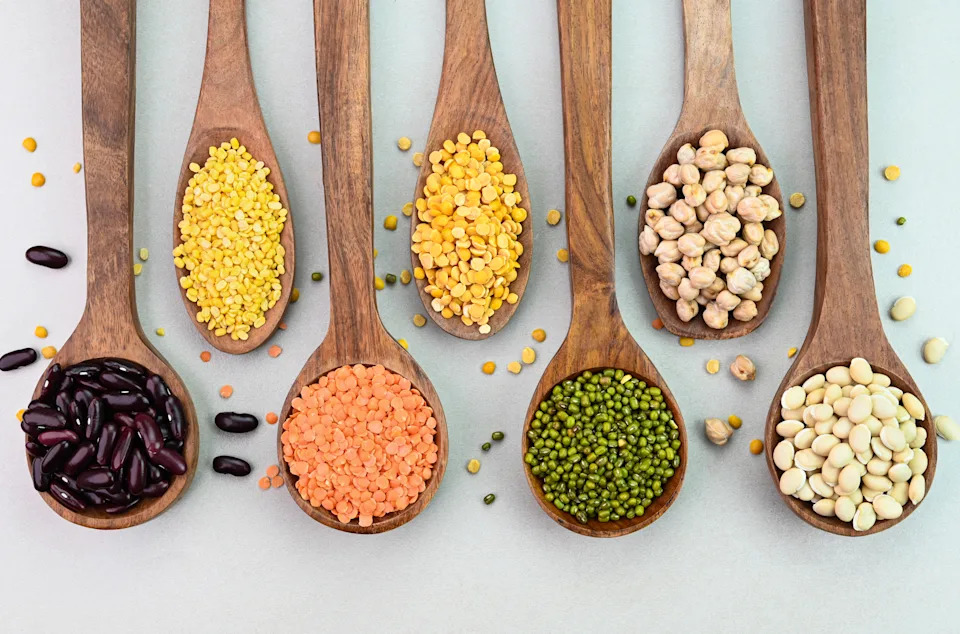 Variety of lentils and pulses in wooden spoons on a white background.