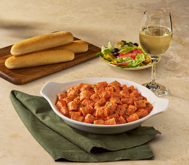 a meal setup with pasta breadsticks salad and wine