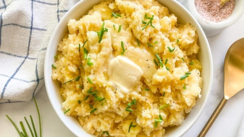 Bowl of mashed potatoes topped with butter and chopped chives