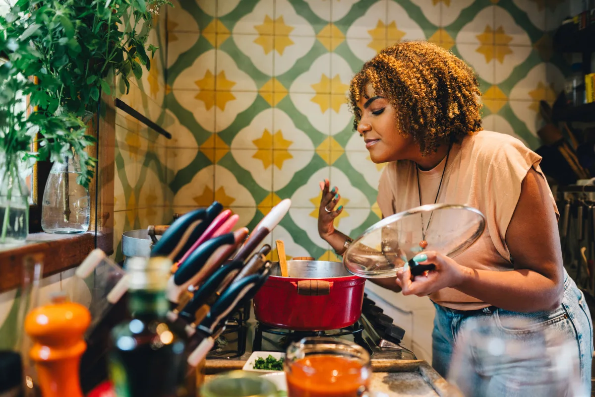 Woman smiling with her eyes closed while smelling food cooking in a pot on a stove in her kitchen at home