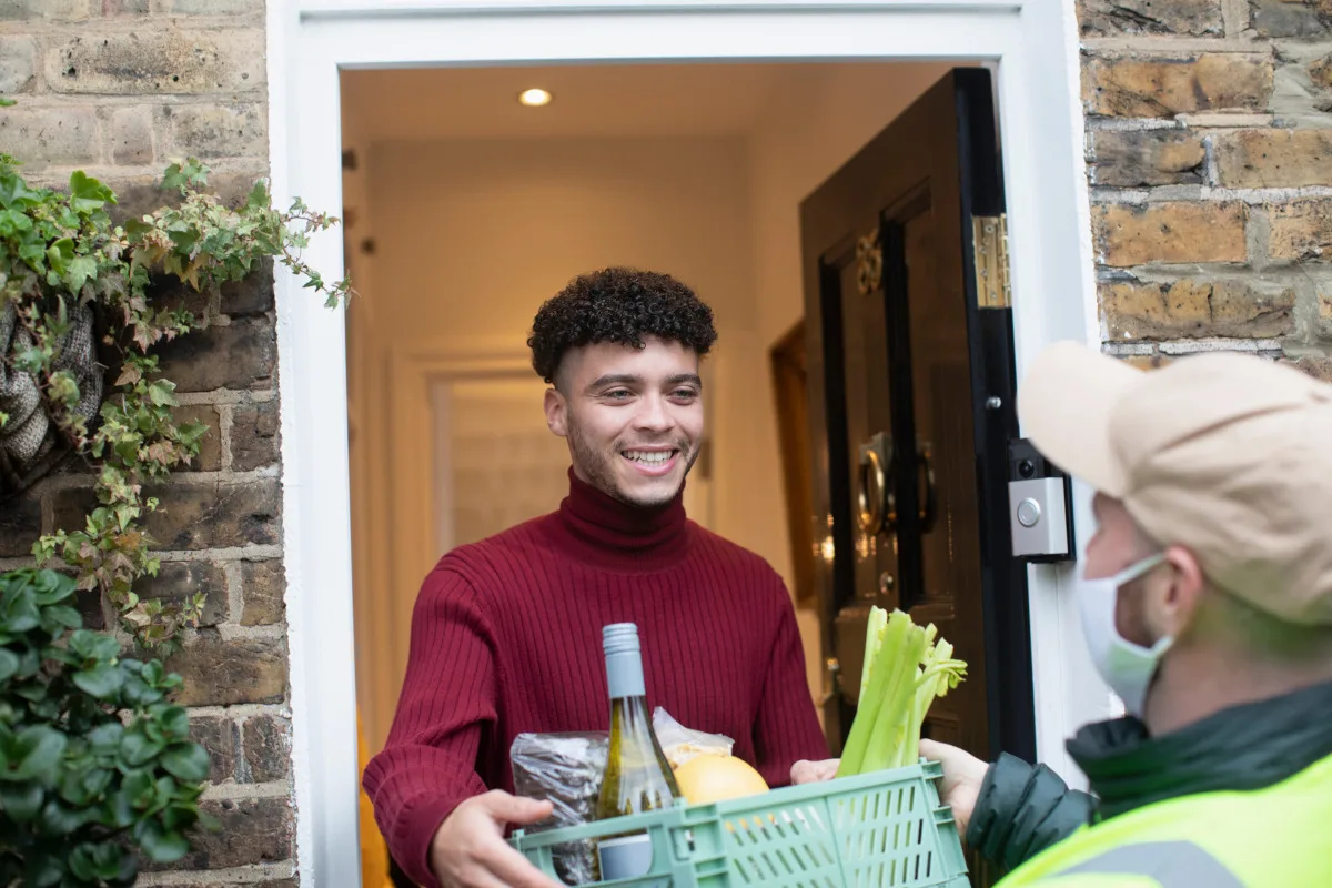 Happy man receiving food grocery delivery from delivery man in face mask at front door of home