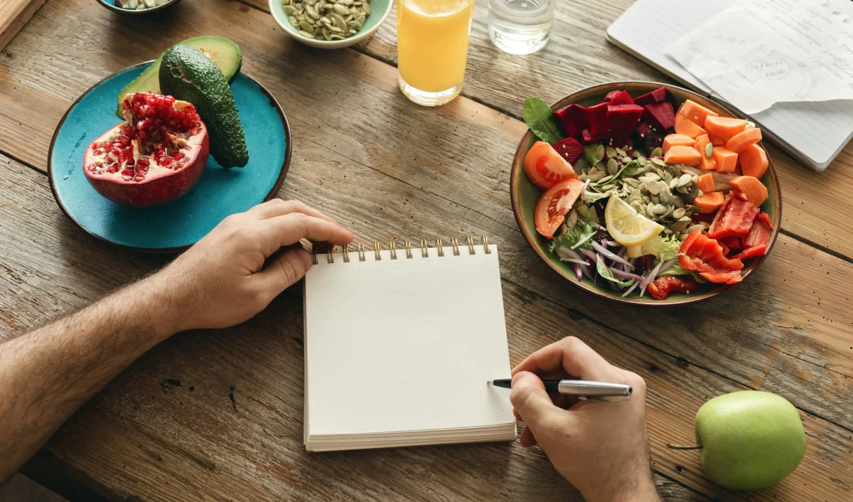 First-person POV photo of a person writing a list on a notepad, surrounded by healthy foods