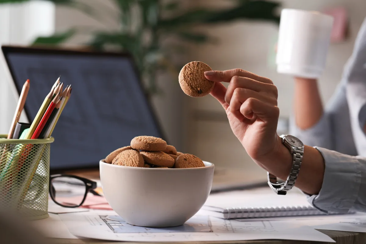 Close up of businesswoman taking cookie from a bowl while working in the office.