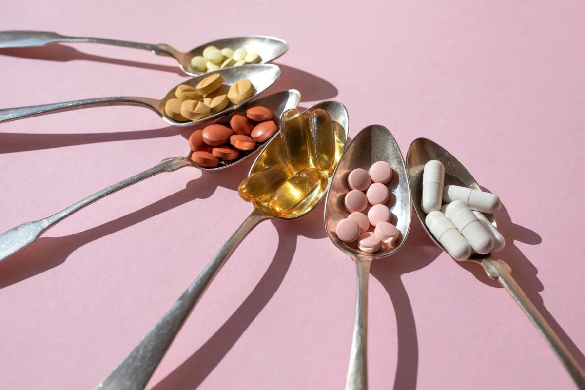 Various spoons with pills and tablets on the pink background