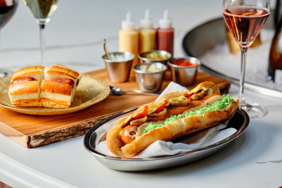 A fancy hot dog with Champagne glasses on the side.