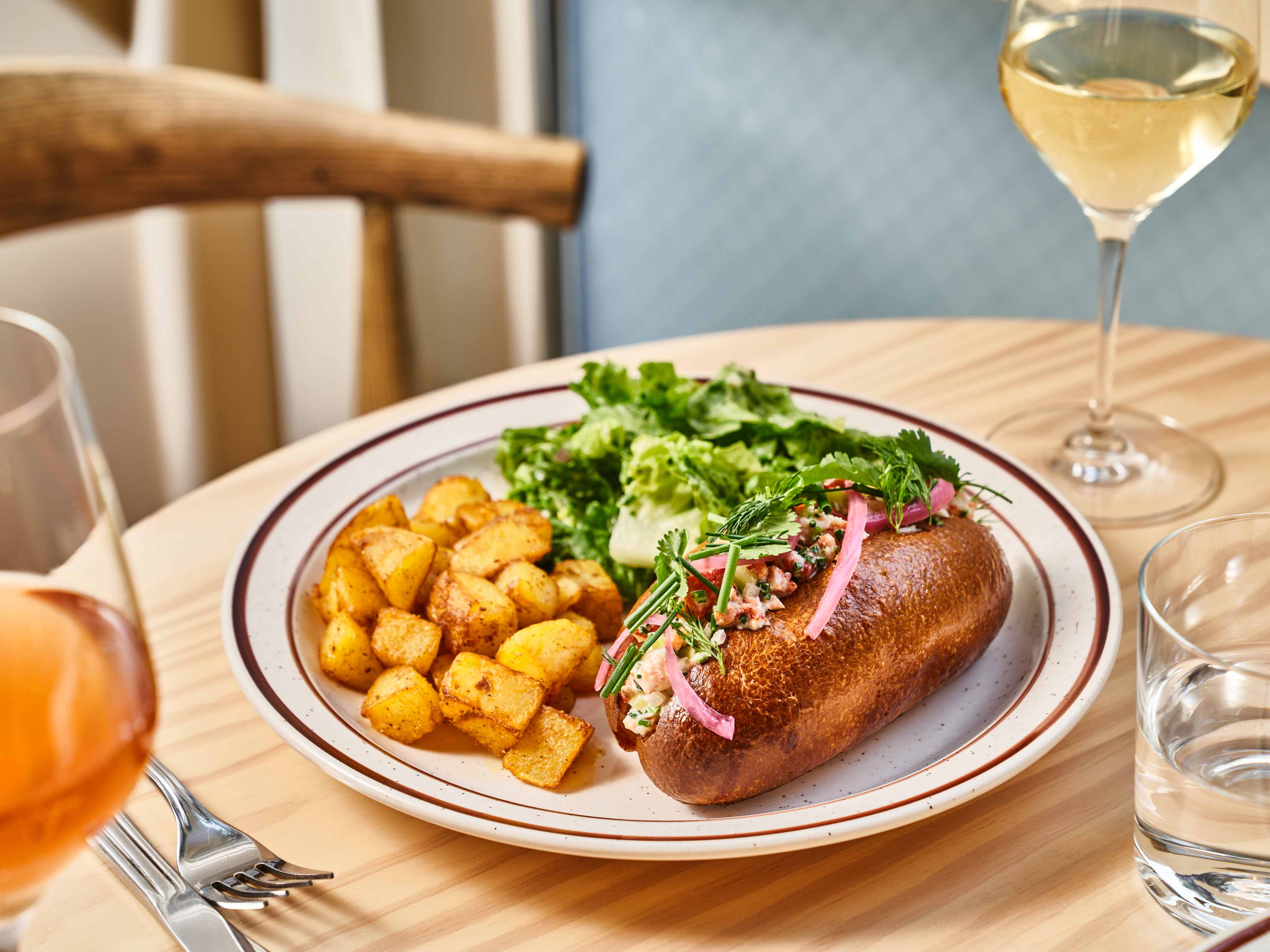 lobster roll with potatoes and side salad on plate
