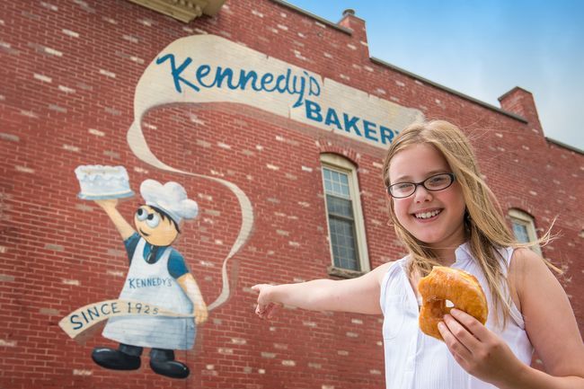 girl holding donut and point to mural on side of building for Kennedy's Bakery in Cambridge, Ohio