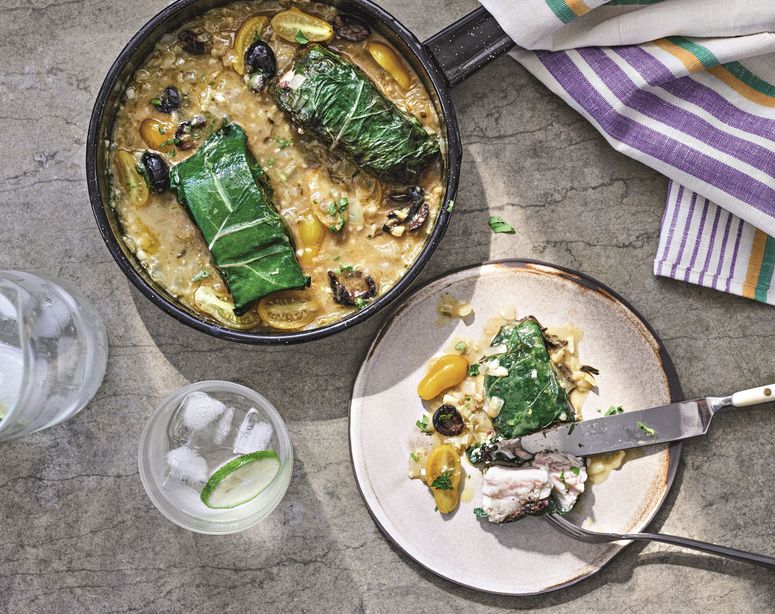 Top view of skillet filled with chardwrapped fish fillets with lemon and olives in light brown sauce.