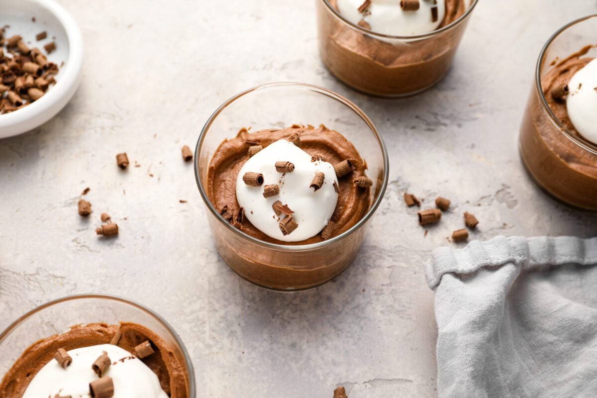 glasses of chocolate mousse topped with sweetened whipped cream and chocolate shavings 