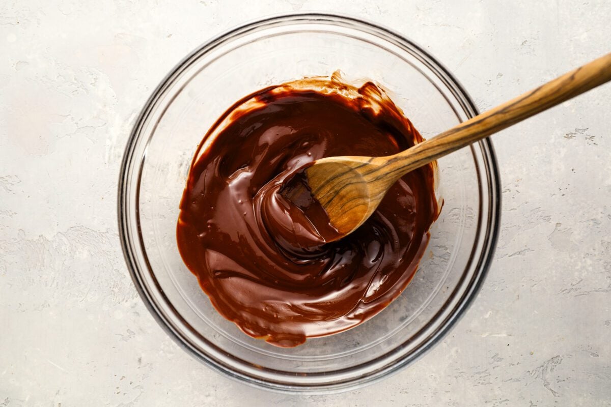 melted butter and chocolate mixed together with wooden spoon in medium glass bowl