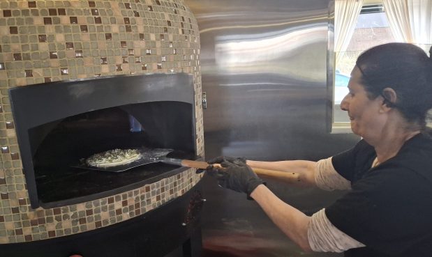 Hilana Yousef, chef/manager of the new Cafe Zaytun in Elgin, places a flatbread pizza she just made into the restaurant's brick oven. (Mike Danahey/The Courier-News)