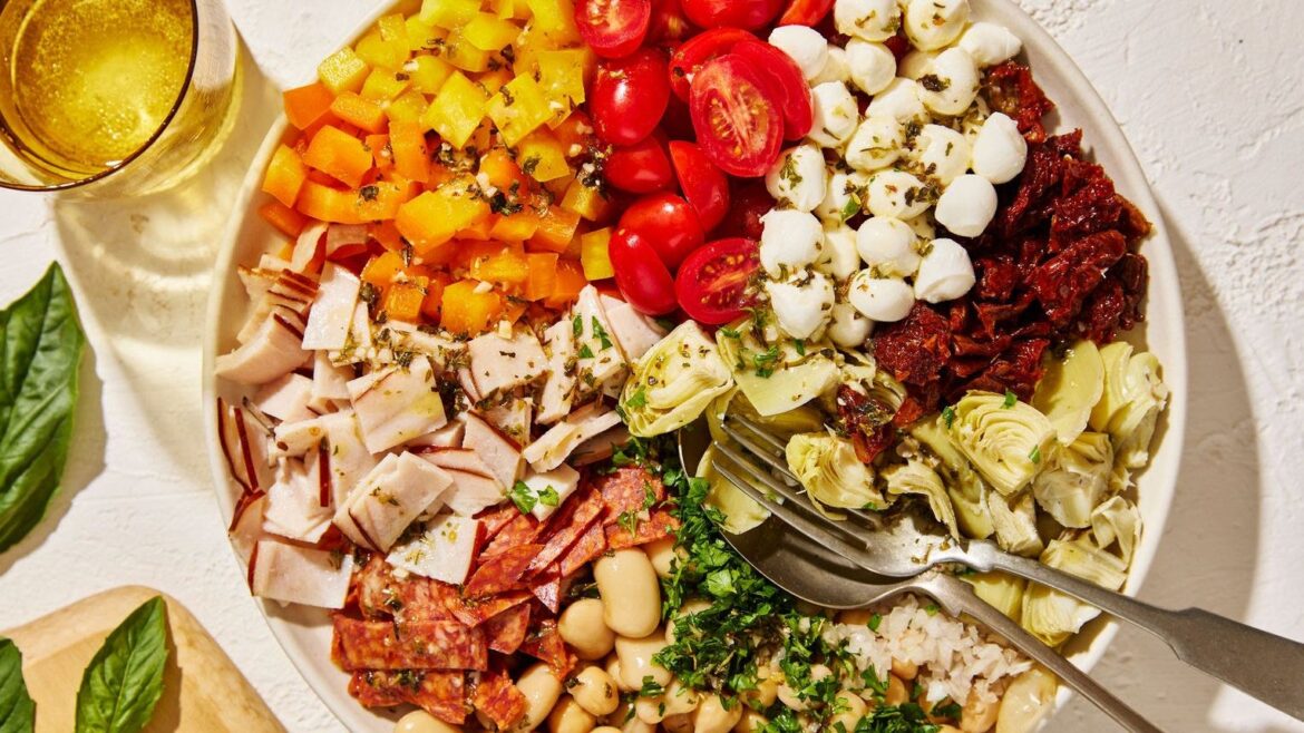 Bowl of ingredients in a pie chart arrangement, including cherry tomatoes, mozzarella balls, sundried tomatoes, artichokes, white beans, pepperoni, deli meat and chopped orange and yellow peppers