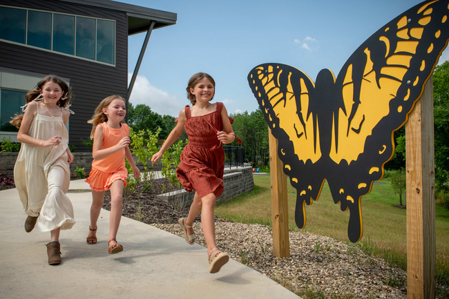 three young girls skipping past large yellow butterfly cutout to follow the trails at the Eco-Discovery Center at Salt Fork State Park in Cambridge, Ohio