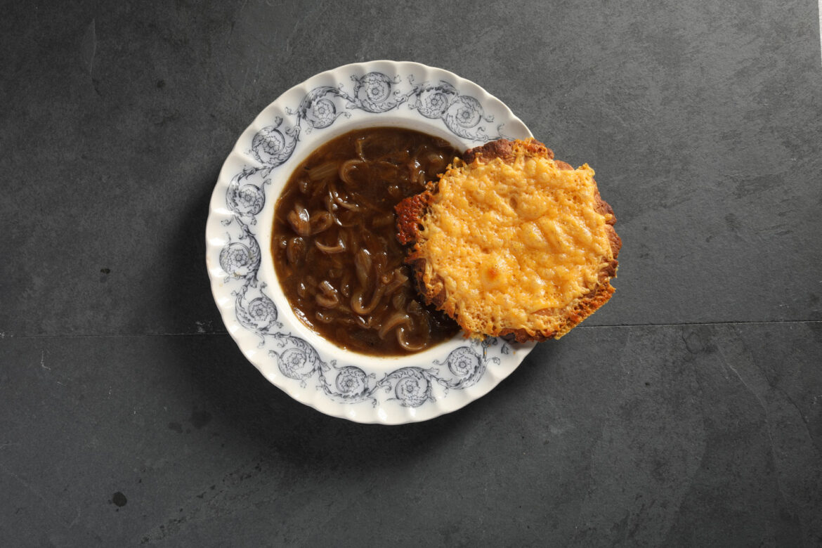 A bowl of french onion soup with a cheese touille in a white bowl with blue designs.