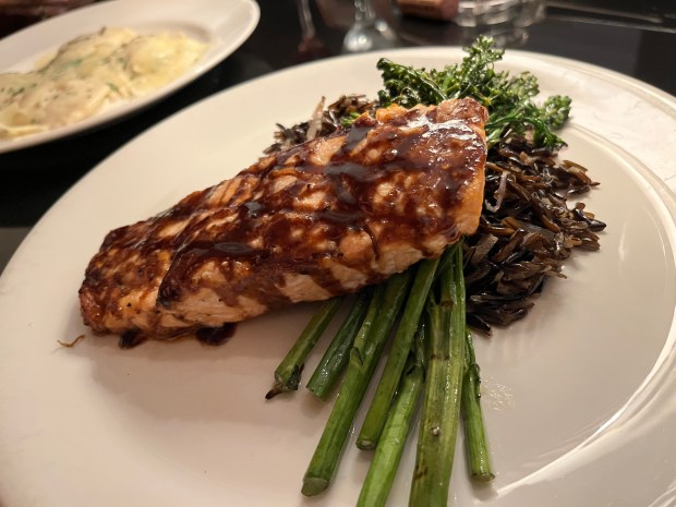 Fish atop bright green broccolini and a pile of wild rice. There's a plate of ravioli in the background