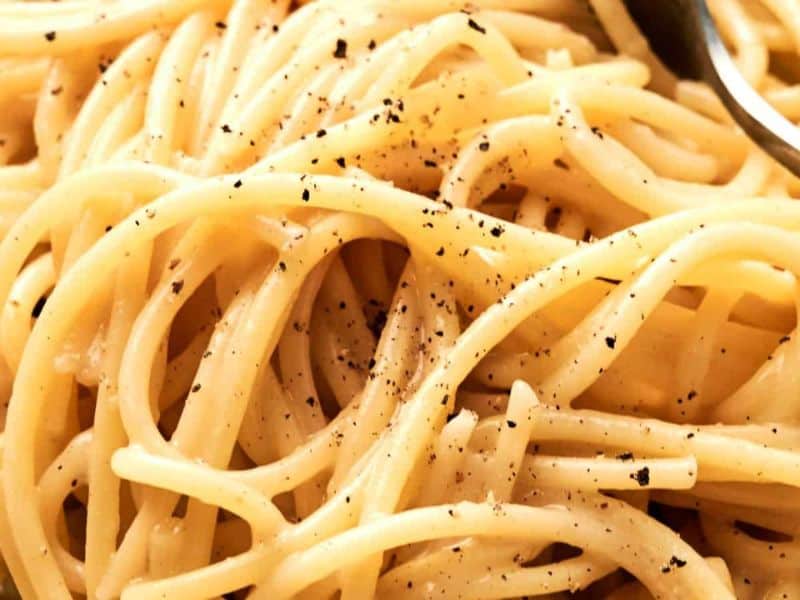 Close-up of cooked spaghetti with cracked black pepper and a fork partially visible.