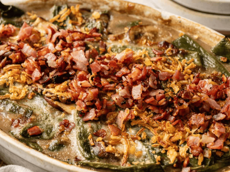 A baked casserole topped with chopped bacon, crispy onions, and melted cheese, featuring visible green peppers and a creamy sauce.