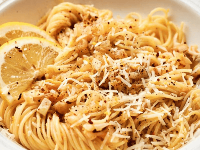 A bowl of pasta with lemon slices and parmesan cheese.