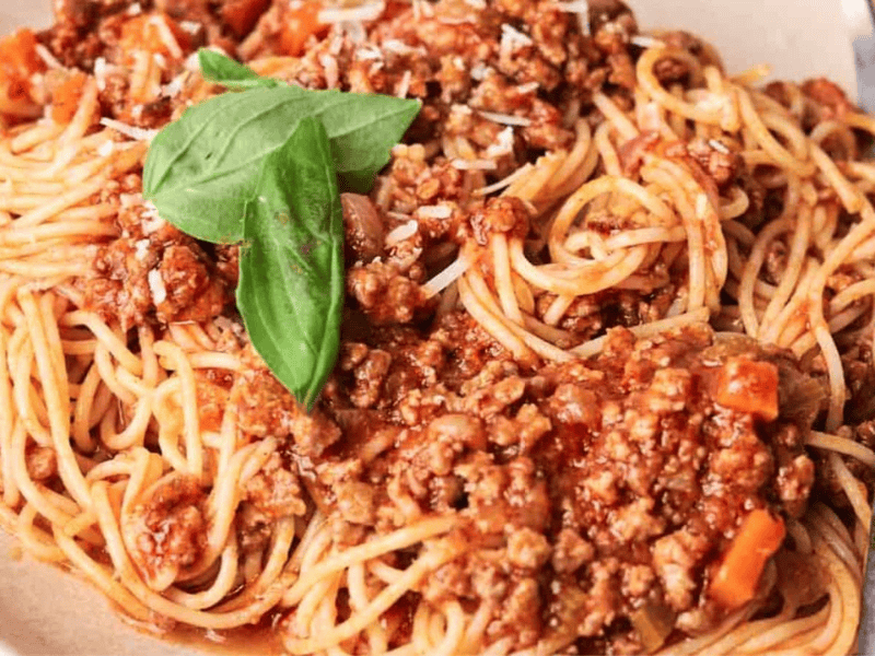 A plate of spaghetti topped with meat sauce and a fresh basil leaf, accompanied by a fork on the side.