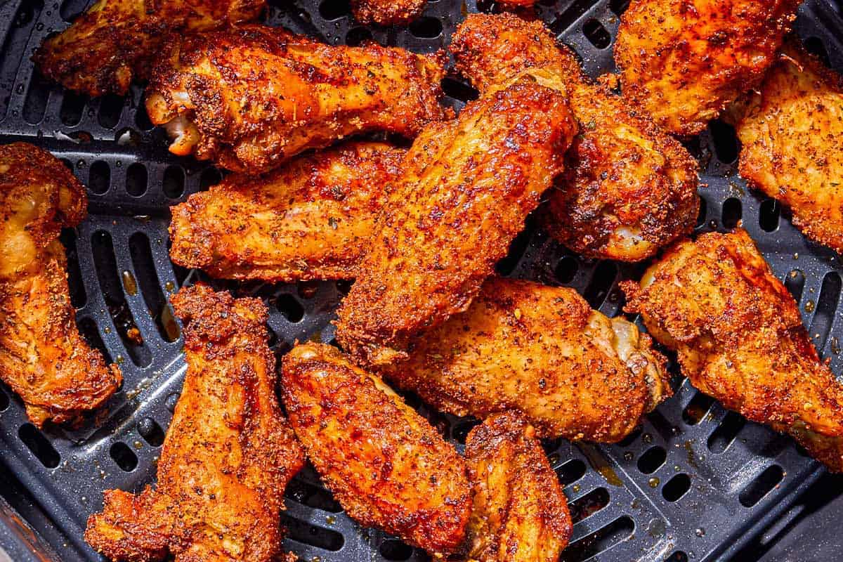 Seasoned air fryer chicken wings in a basket of an air fryer.