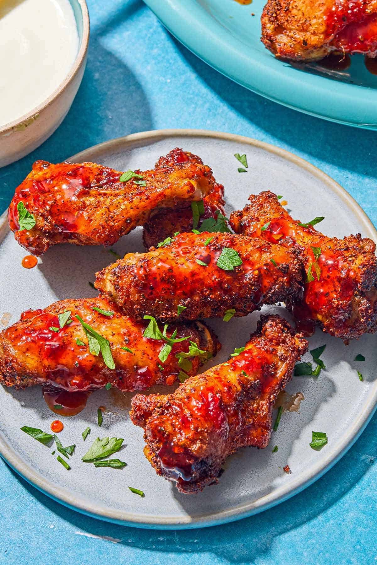 A close up of six air fryer chicken wings topped with harissa hot honey and chopped parsley on a plate.