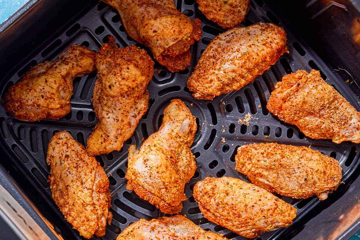 Uncooked seasoned air fryer chicken wings in a basket of an air fryer.