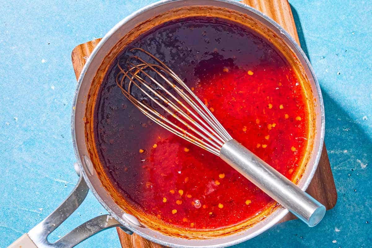 The harissa hot honey for the air fryer chicken wings in a saucepan with a whisk.
