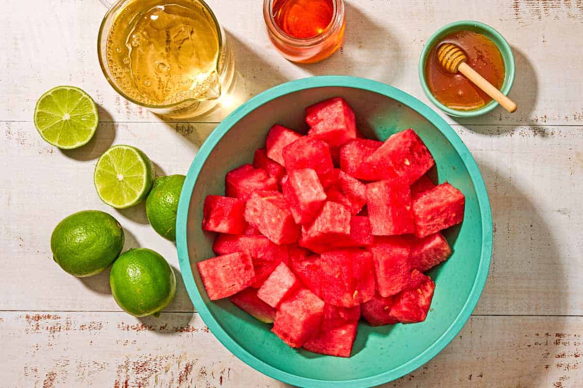 Ingredients for watermelon sangria including cubed watermelon, honey, limes, white wine, and gran marnier.