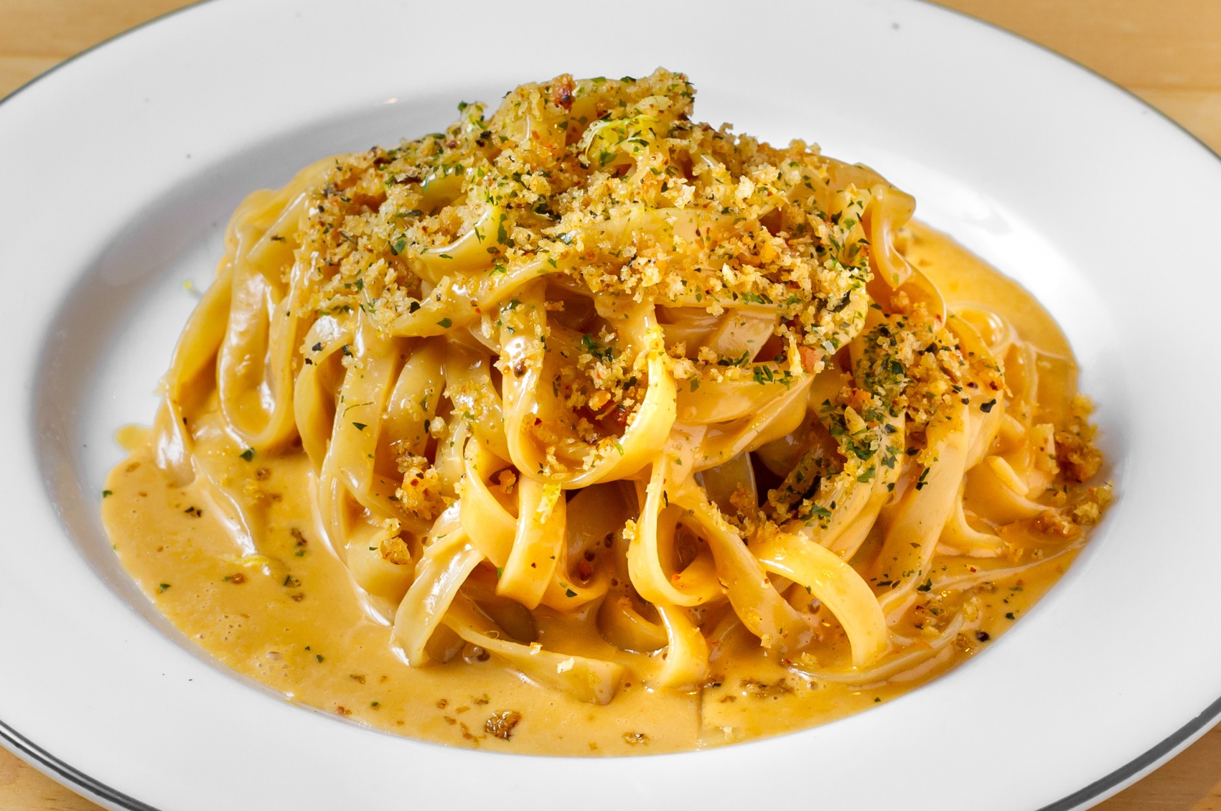 a sideview image of a plate of uni pasta. the sauce is glossy and slightly orange, covering tagliatelle noodles. the pasta is finished with breadcrumbs.