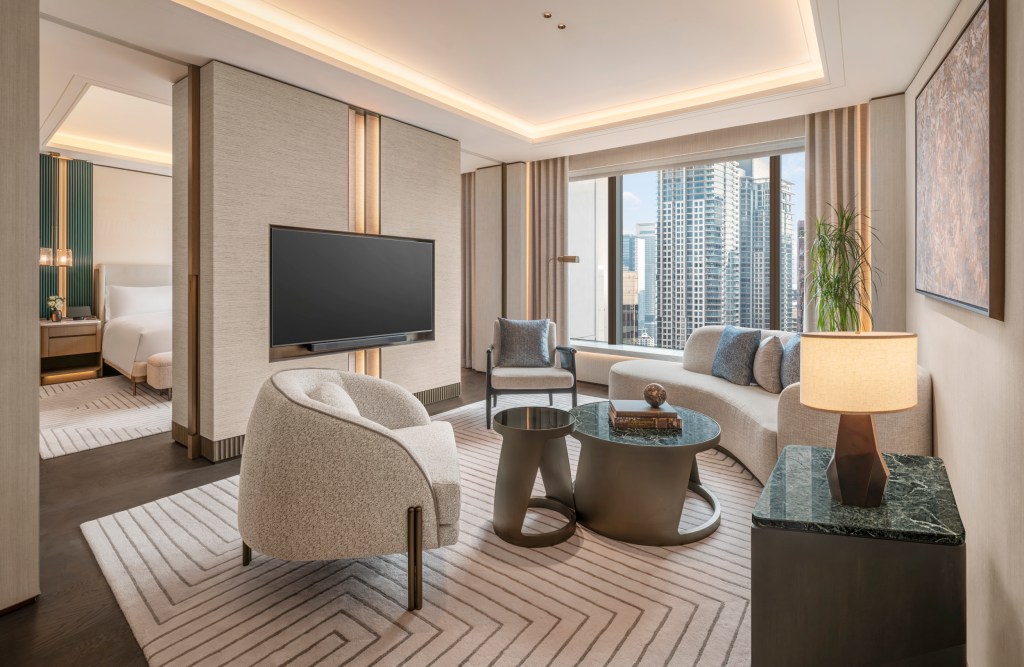 Living room with a curved sofa accent pillows and two armchairs with black marble-top coffee tables on a light beige rug with a geometric pattern.
