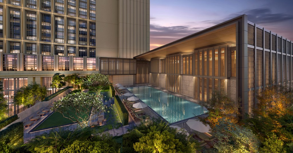Modern outdoor pool at dusk beside a glass-front building, with lounge chairs, umbrellas, landscaped gardens, and soft lighting under a purple sunset sky.