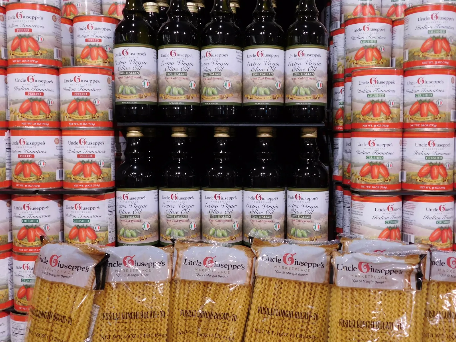 Cans of tomato sauce, containers of olive oil and bags of dry pasta on display on an endcap at a grocery store